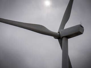 Close-up of a wind turbine on a foggy day, sun behind the clouds, dark and grey image