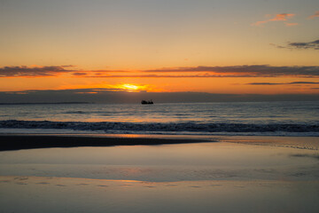 Fototapeta na wymiar Sunrise over the sea with sky reflection on the shore and a ship on the horizon
