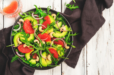 Healthy vegan vegetarian lunch salad with arugula, avocado, grapefruit and cashews and dressing of olive oil, honey and wine vinegar. White rustic kitchen table, top view