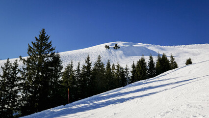 Blue sky over a snowy alpine ski slope lined with trees  - 488317709