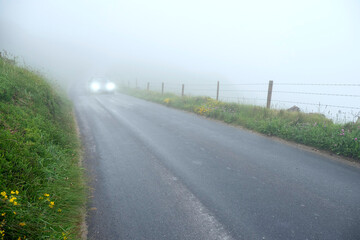 Car with headlights on on a small asphalt country road in a fog. Road safety and travel in dangerous weather conditions concept.