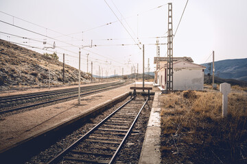 electrified railroad tracks with a curve in the background, in front of an abandoned train station,...