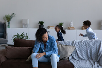 Unhappy nervous young African American mother or nanny feeling tired of naughty noisy little...