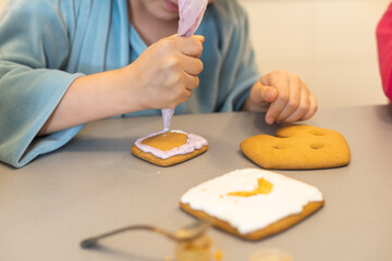 Close up view of kids hands decorating homemade cookies for holidays. A child decorates cookies...