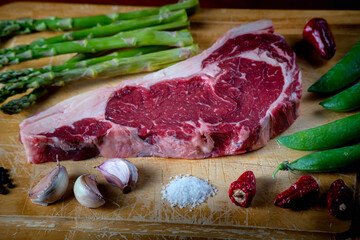 beef on a wooden board accompanied by asparagus, green beans, garlic, chili peppers, salt and peppercorns. Food photo