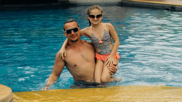 The father with little daughter have fun in the pool. Dad plays with the child. The family enjoy summer vacation in a swimming pool jumping, spinning, splash water. Slow motion.