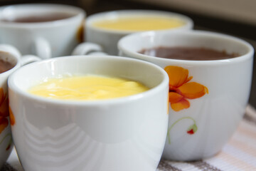 close-up shot of porcelain cups filled with yellow vanilla and brown chocolate flummery
