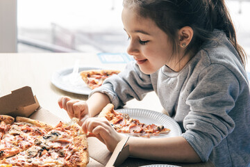 Happy little girl looks at pizza with appetite.