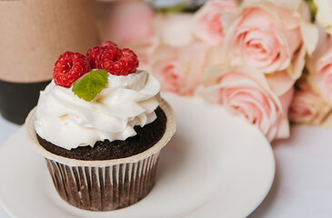 Chocolate muffin with cream and raspberries on a white plate.