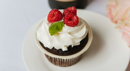 Chocolate muffin with cream and raspberries on a white plate.