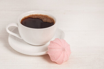 Espresso in a white cup and one meringue on a wooden table.