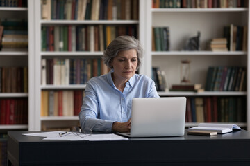 Thoughtful old senior business woman entrepreneur looking at computer screen, studying or working distantly on project, considering problem solution, analyzing data preparing presentation or document.