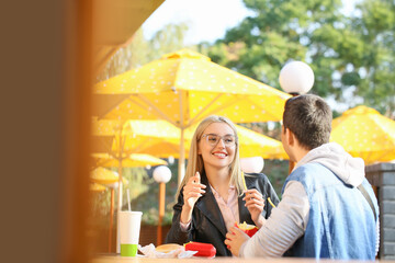 Young couple eating french fries in cafe outdoors