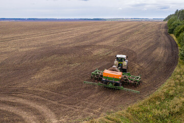 Obraz premium Aerial view of agricultural tractor with seeder machine at work on the field 