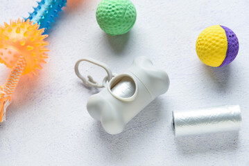 Dispenser with pet waste bags and toys on light background, closeup
