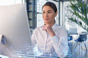 Attractive businesswoman in white shirt at workplace working with laptop to optimize development by implying new technologies in business process. Hi tech hologram over office background