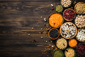 Legumes, lentils, chikpea and beans assortment in different bowls on wooden table. Top view with...