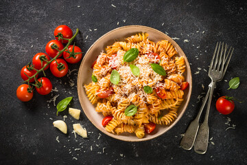 Italian pasta alla arrabiata with basil and parmesan cheese on dark table. Fusilli pasta with tomato sauce arrabbiata. Top view.