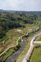 Fototapeta na wymiar Aerial view of paddy field and road by small river of countryside in Indonesia with clouds in blue sky background.