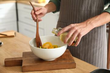 Young man pouring oil into bowl with salad in kitchen, closeup