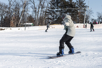 A male snowboarder is snowboarding down a snowy slope, looking at the camera and waving his hand.