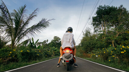 Love couple on red motorbike in white clothes to go on forest road trail trip. Two caucasian tourist woman man drive on scooter. Motorcycle rent, safety helmet, sunglasses. Asia Thailand ride tourism.