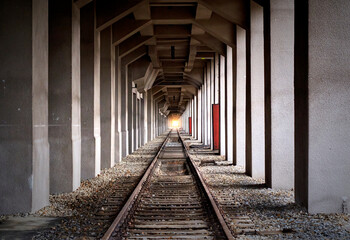Endless rails in central perspective between close standing concrete pillars with light in vanishing point of perspective