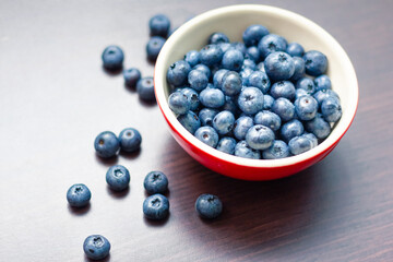 Blueberries in a red bowl on wooden table.