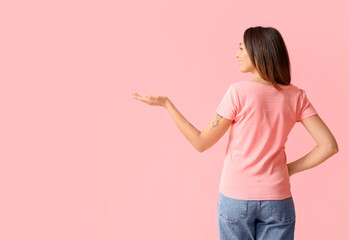 Young woman in blank t-shirt showing something on color background, back view