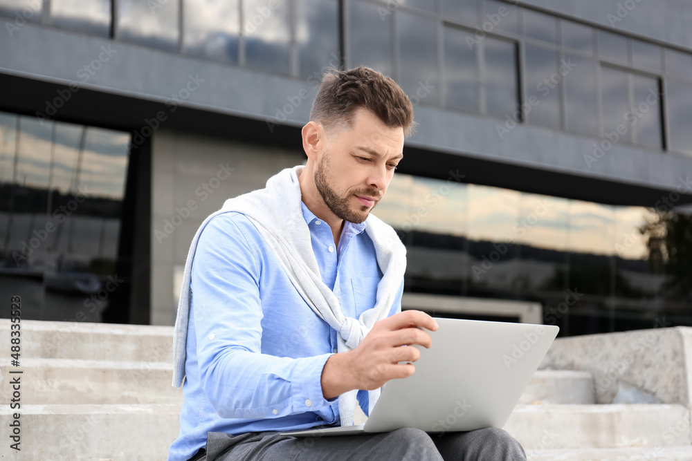 Wall mural Handsome businessman working with laptop outdoors