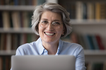 Head shot portrait of beautiful smiling middle aged businesswoman in eyewear working remotely on...