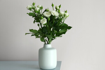 Vase with bouquet of beautiful fresh roses on table near white wall