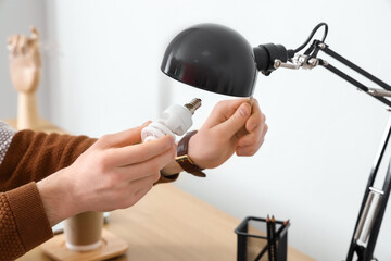 Man changing light bulb in black lamp at workplace, closeup