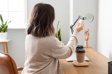 Woman changing light bulb in black lamp at workplace
