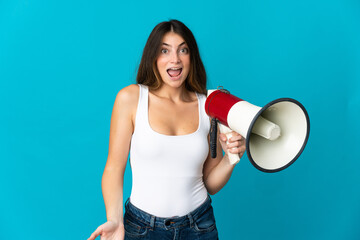 Young caucasian woman isolated on blue background holding a megaphone and with surprise expression