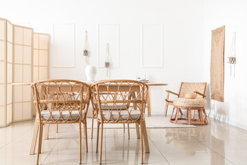 Interior of light dining room with table, wicker chairs and folding screen
