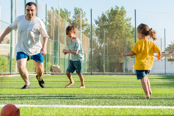 Obraz premium Full body man playing football with children on green lawn. Father's Day concept. 
