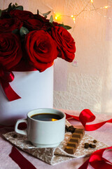 Coffee in a white cup with milk chocolate on the table against the background of red roses