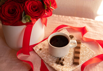 Coffee in a white cup with milk chocolate on the table against the background of red roses