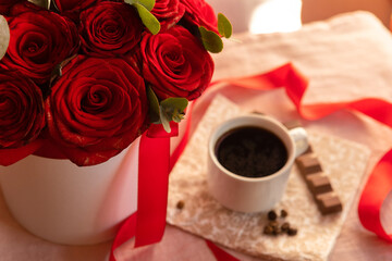 Obraz na płótnie Canvas Coffee in a white cup with milk chocolate on the table against the background of red roses