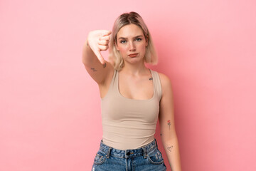 Young caucasian woman isolated on pink background showing thumb down with negative expression