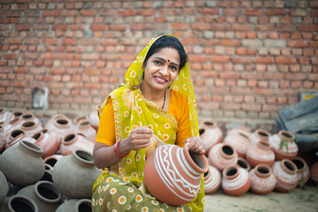 Portrait of happy traditional Indian woman potter artist painting and decorating design on clay pot...