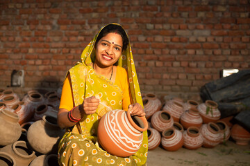 Portrait of happy traditional Indian woman potter artist painting and decorating design on clay pot. Small Business Owner, handicraft, skill india.