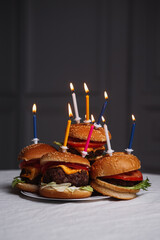 A vertical photo of burgers lying on a plate the white table on a gray background with birthday candles in them