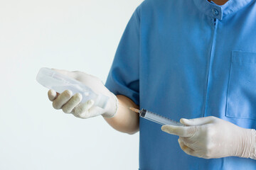 Hands of a doctor or nurse wearing rubber gloves and using a syringe to suck Sodium Chloride in a clinic or hospital.