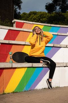 Retrato de una alegre mujer con un monopatín en unas escaleras de colores