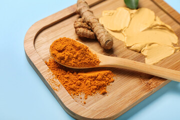 Board with turmeric mask and powder on blue background, closeup