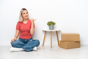 Young woman moving in new home among boxes isolated on white background pointing to the side to present a product