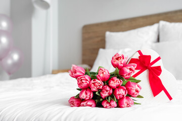 Bouquet of tulip flowers with gift on bed