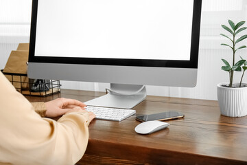 Woman working with modern computer on wooden table near light wall